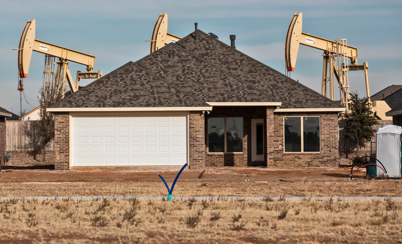 Three oil pumpjacks visible behind a newly constructed house in the Permian Basin