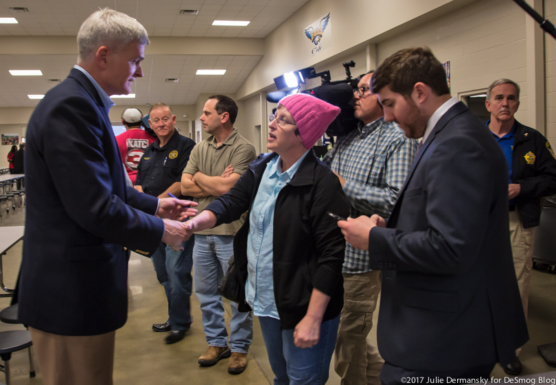 Sen. Cassidy shakes hands with a woman in a pink hat at a town hall meeting.