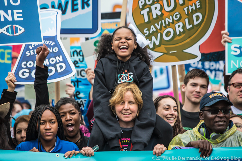 A girl known as Little Miss Flint on the shoulders of marchers at the front of the Science March.