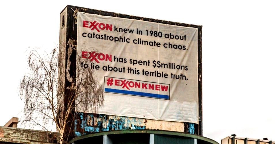 White banner on side of building reads 'Exxon knew in 1980 about catastrophic climate chaos. Exxon has spent $$ millions to lie about this terrible truth. #ExxonKnew'