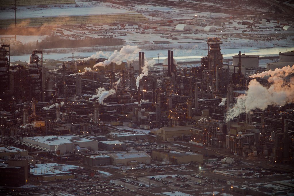 An oil refinery with smoke pouring out of smokestacks and snow on ground in the background