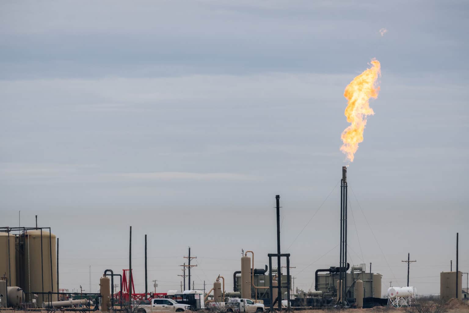 A methane flare burning at an oil and gas site with various tanks and pipes in the Permian Basin