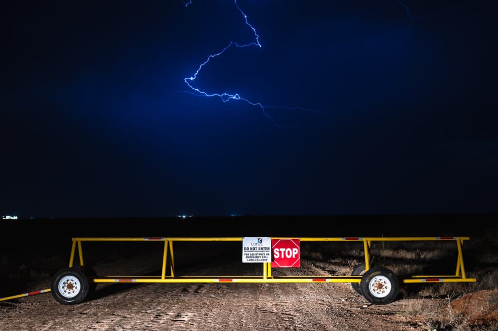 Lightning strikes over Lotus LLC disposal facility mobile gate with a stop sign over a dirt road.