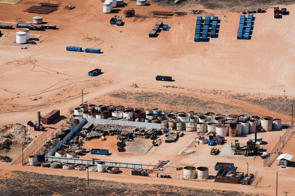 Aerial view of industrial site with dozens of open tanks of oilfield waste and barrels stacked up in the desert