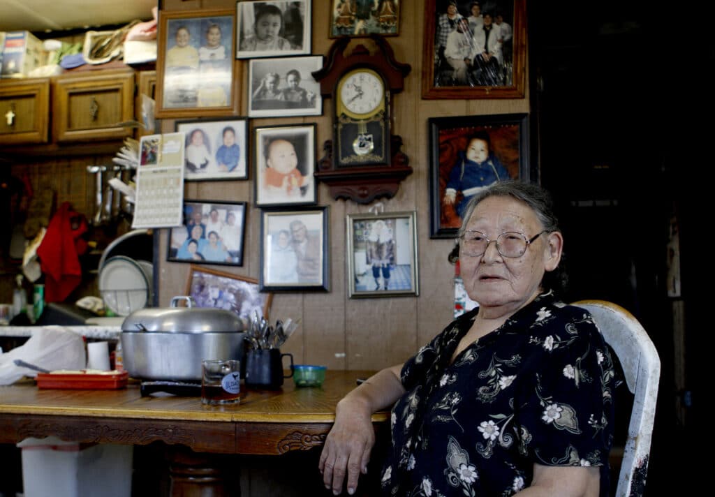 Lucy Adams sits at a table in front of a wall of family photos