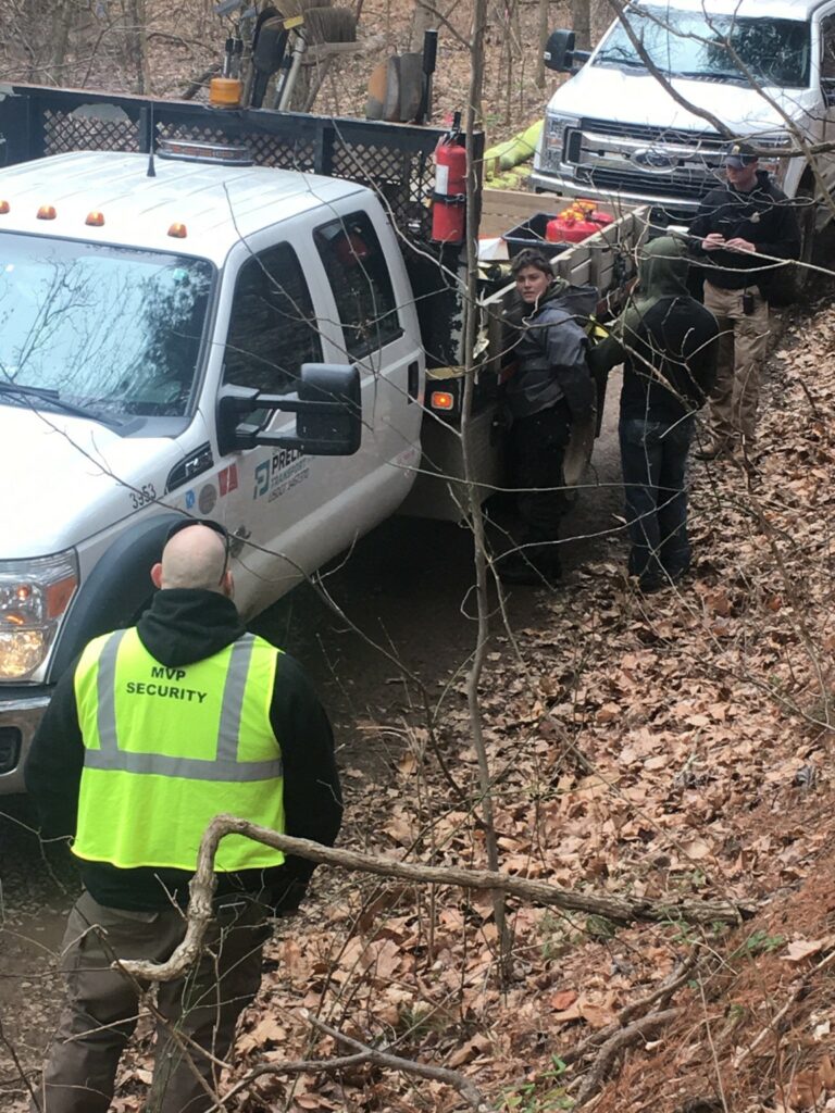 A pipeline protester is handcuffed by a security officer against a Precision Pipeline truck while two other officers stand nearby, one wearing a yellow vest reading 'MVP Security'