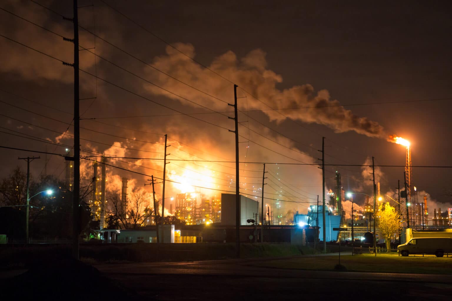 A bright fiery flare lights up a smokey sky over the industrial site of a Shell refinery.