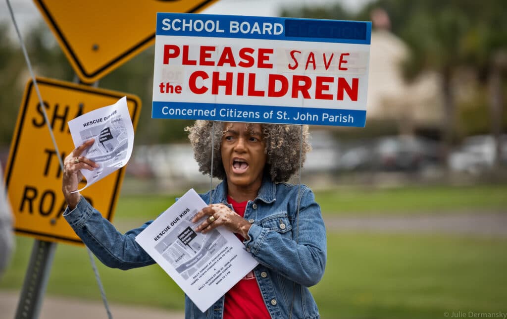 A Black woman with gray in her hair holds signs and flyers about saving children from air pollution while standing outside.