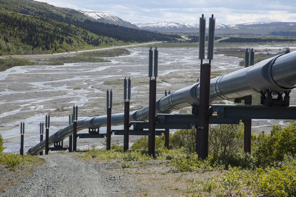 A pipeline system raised above ground goes downhill toward a meandering shallow river with far-off mountains