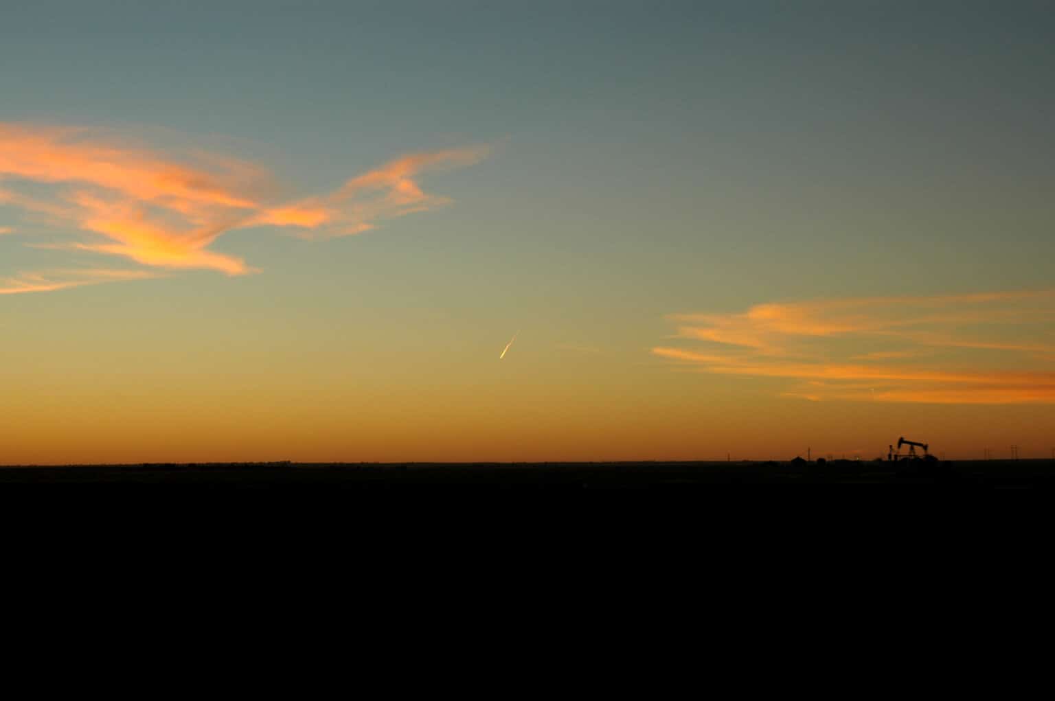 Oil pumpjack in the distance at sunset in a flat plain