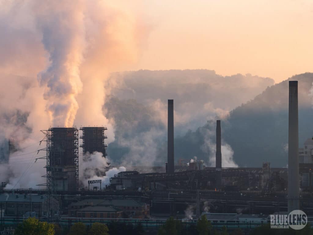 An industrial coke works with thick white smoke billowing out of smokestacks at twilight.