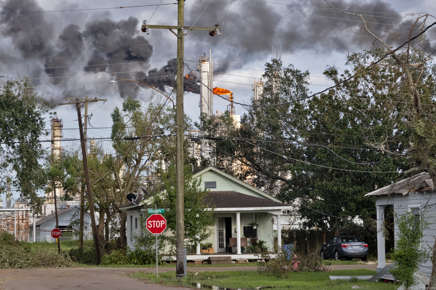 Green house with trees and black smoke coming from a burning refinery flare
