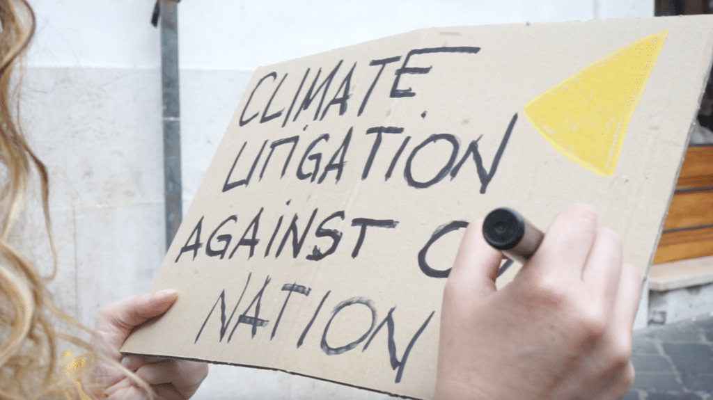 Activist writes 'climate litigation against our nation' on a cardboard sign