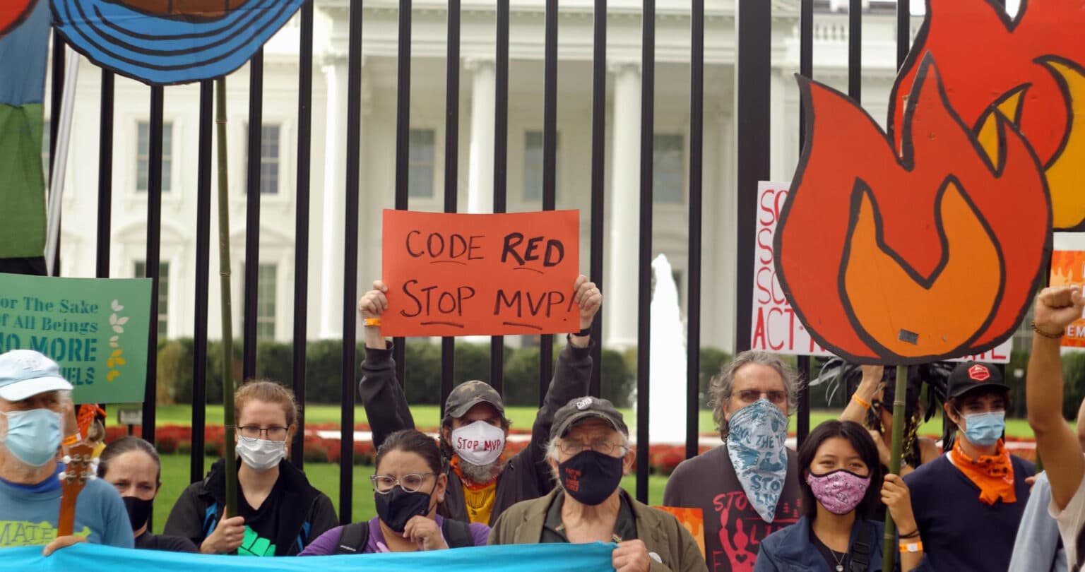 A group of activists hold colorful signs protesting fossil fuel projects in front of the black fence and the White House