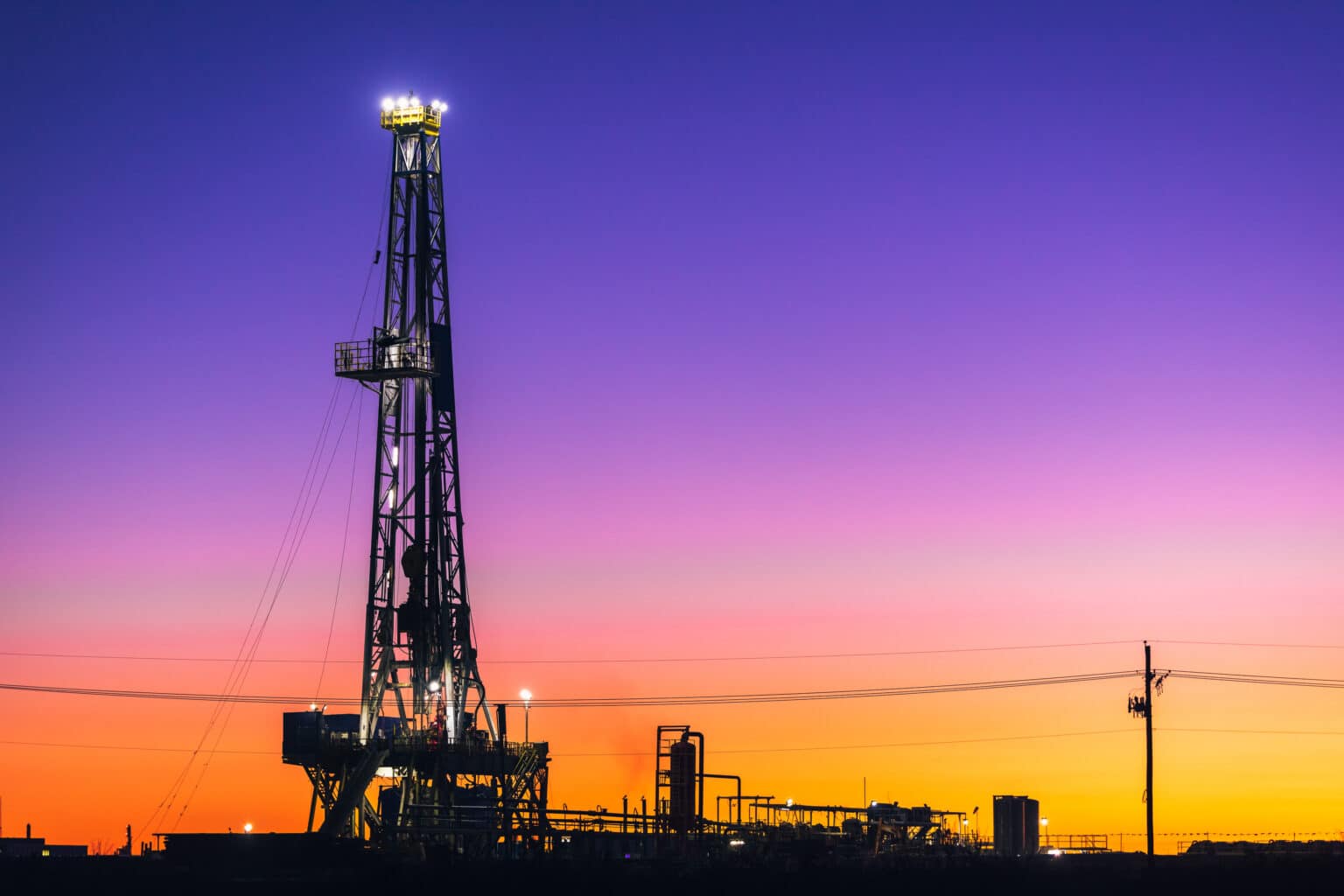 An oil rig is silhouetted against a sunset.