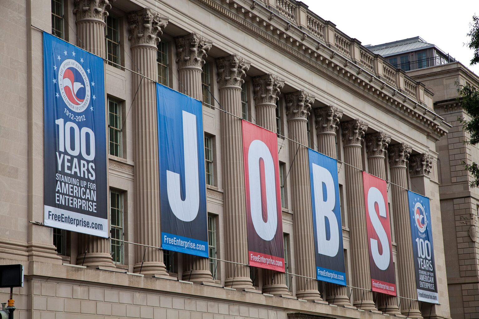 U.S. Chamber of Commerce building with Roman columns and white stone building facade with alternating red and blue banners spelling 'JOBS' and promoting 'American Enterprise'