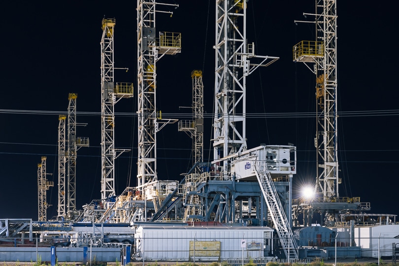 Dozens of upright white drilling rigs are stacked in a storage yard at night