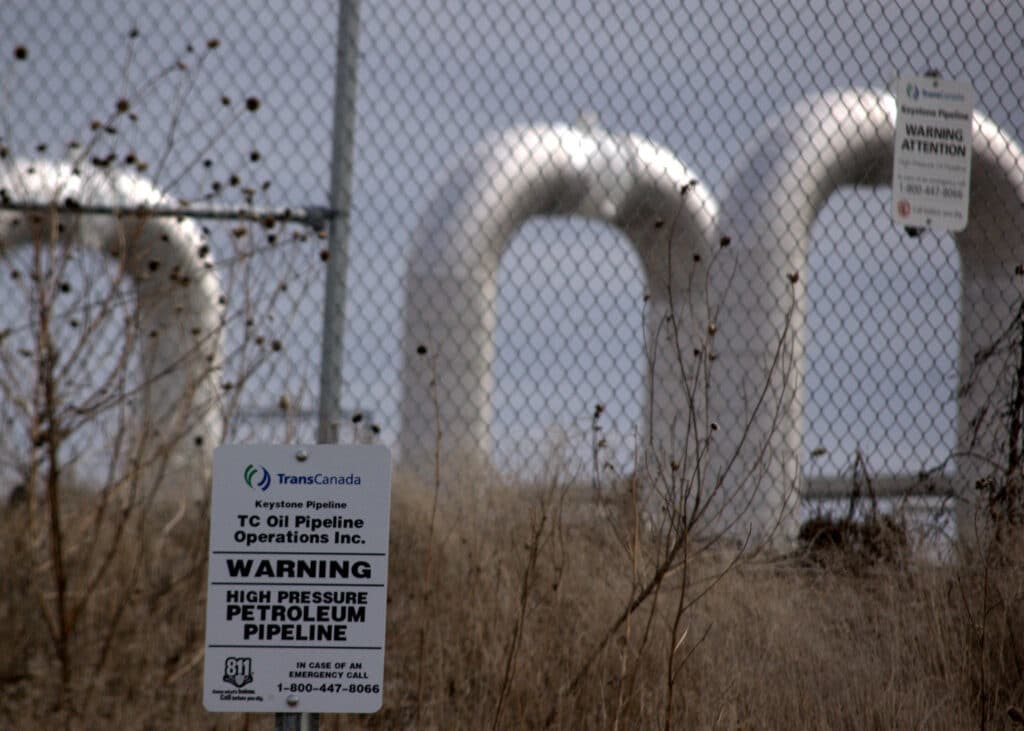 A pipeline pumping station in Nebraska, seen through a fence with a warning sign attached.