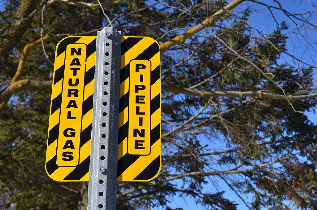 A yellow and black striped signpost reads "Natural Gas Pipeline."
