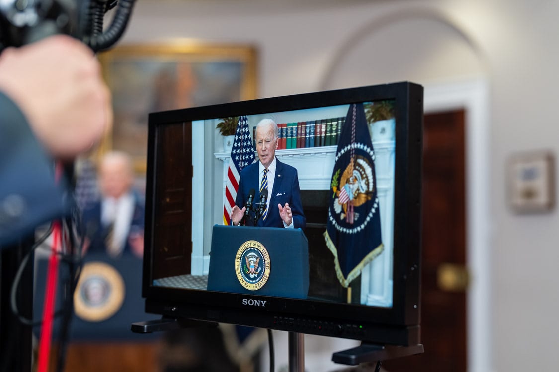 View of monitor showing President Biden at a podium with US flag and seal
