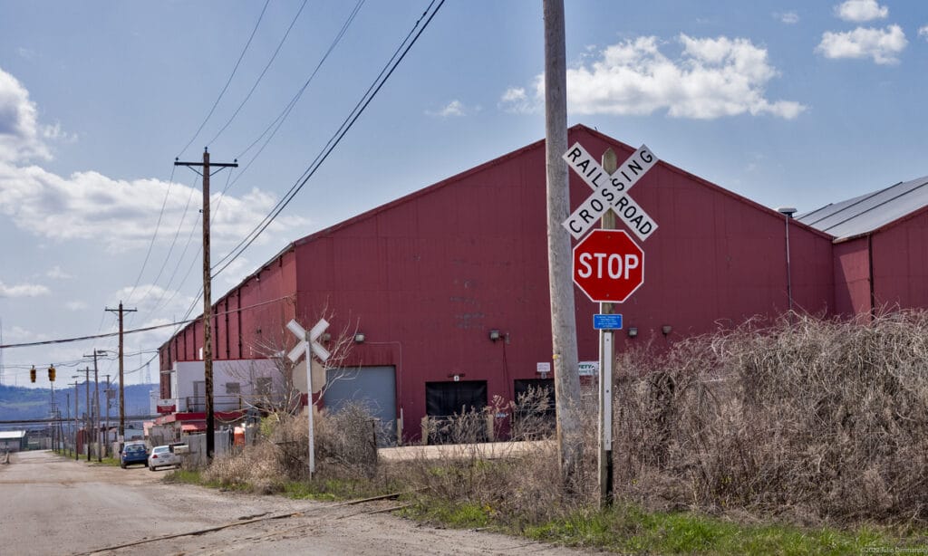 A red warehouse with peaked roof, stop sign with railroad crossing, and powerlines.