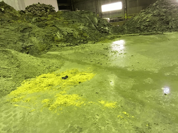 Heaps of indistinguishable grime and waste leak liquid on the dirty flood of an industrial warehouse.