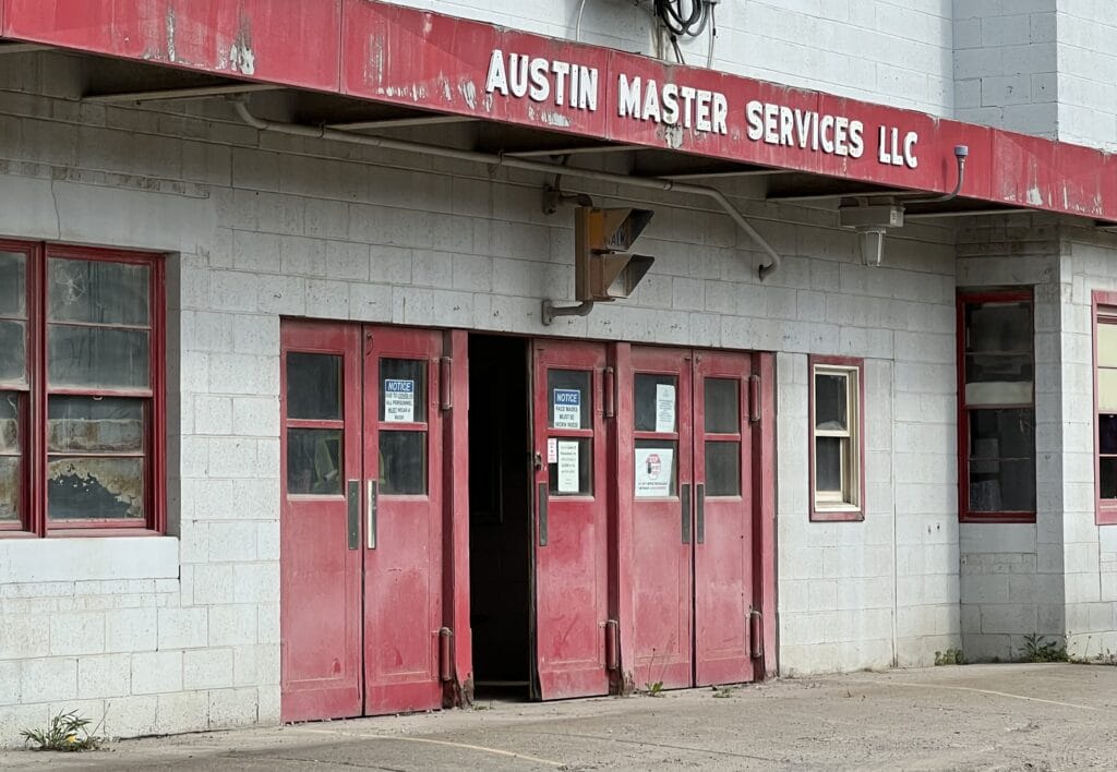 A white cement block building with three sets of red double doors, red-lined windows, and a red trim with the words 'Austin Master Services LLC' in white.