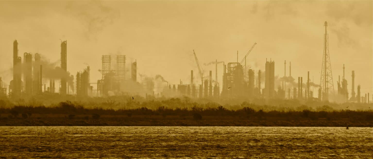 The outline of an industrial waterfront with smokestacks and cranes and a glistening ship canal