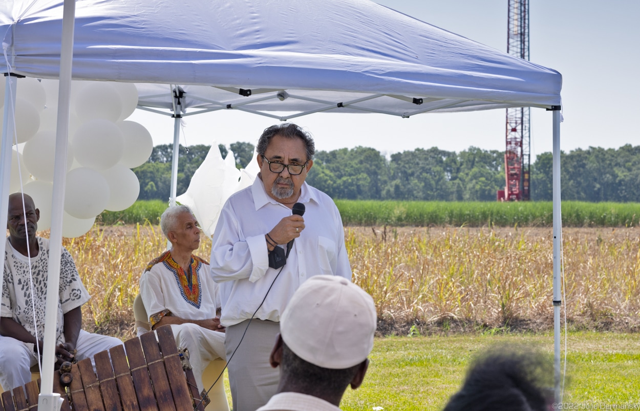 Rep. Grijalva speaks into a microphone under a blue tent in front of a field and construction crane