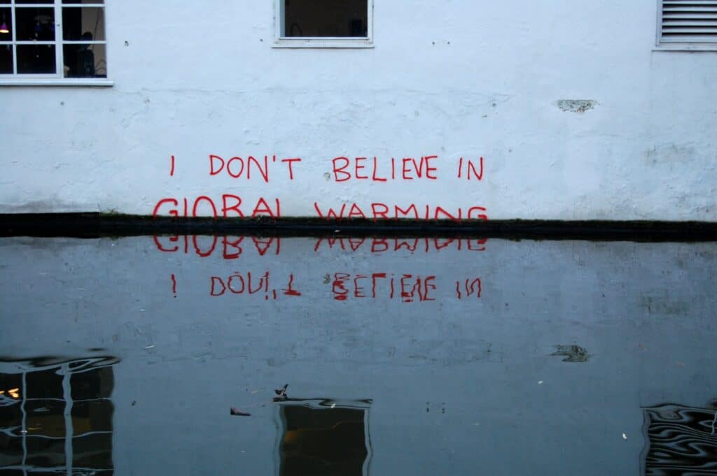 Red spray paint on a white building that says 'I don't believe in global warming' and is reflected in rising water below