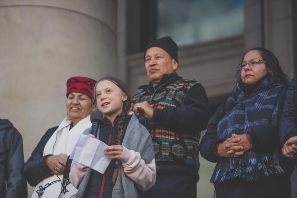 A young woman holds a microphone with three people standing behind her on a building steps