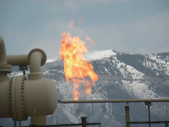 Orange gas flare burning from white pipes in front of a snowy mountain ridge
