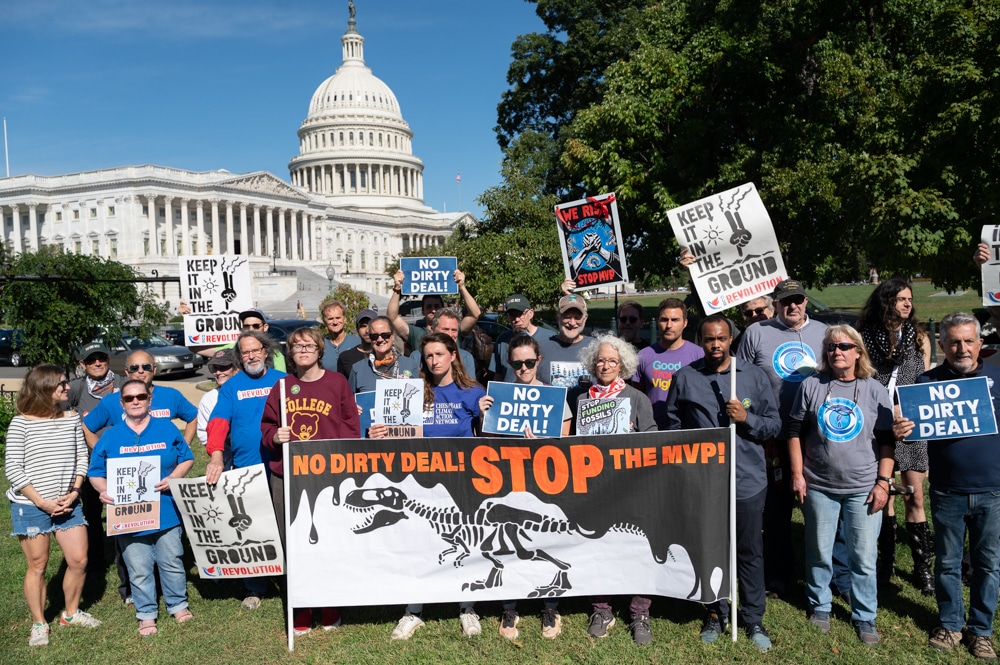 More than two dozen activists hold signs protesting the Mountain Valley pipeline and Sen. Manchin's efforts to greenlight it, standing on the lawn by the US Capitol building.