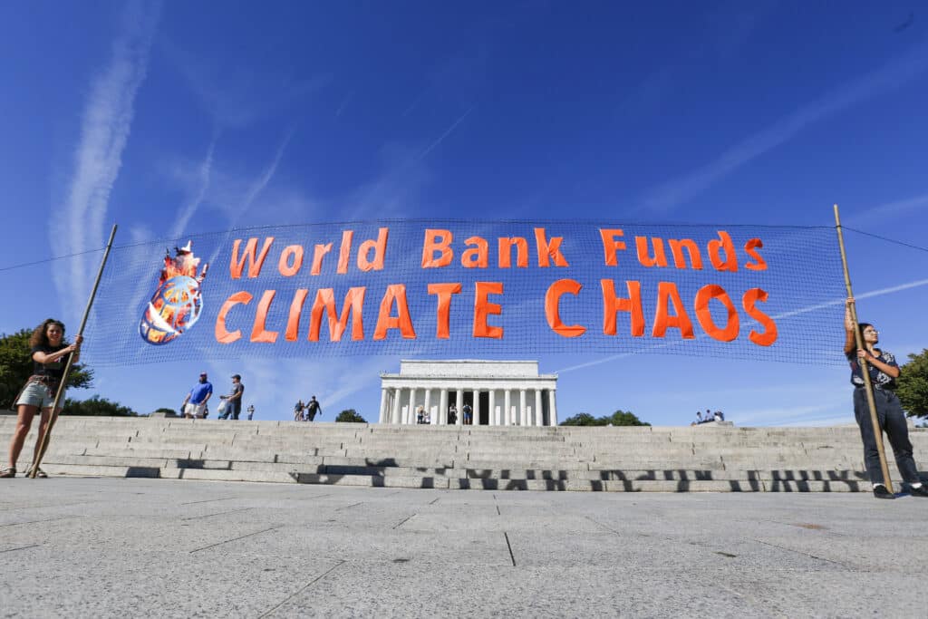 Activitists hold a transparent banner in front of Lincoln Memorial with orange text 'World Bank Funds Climate Chaos'