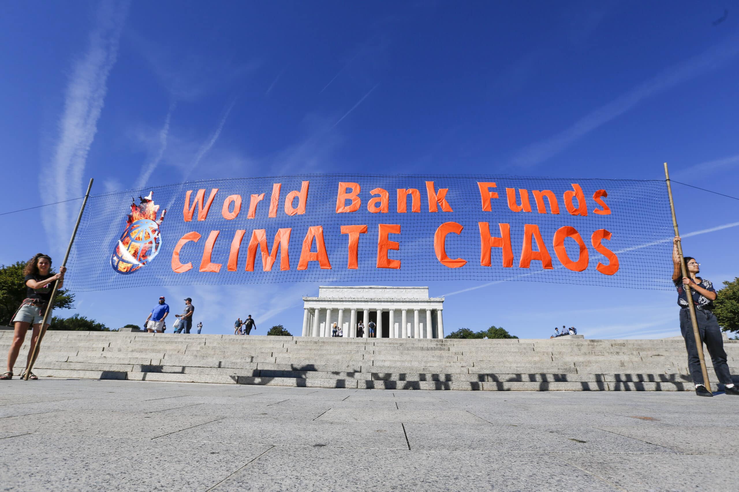 Two activists hold a banner that says "world bank funds climate chaos" in front of the Lincoln Memorial in Washington DC
