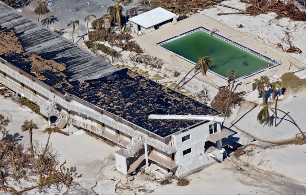 Aerial view of damaged two story hotel next to a debris-filled swimming pool.