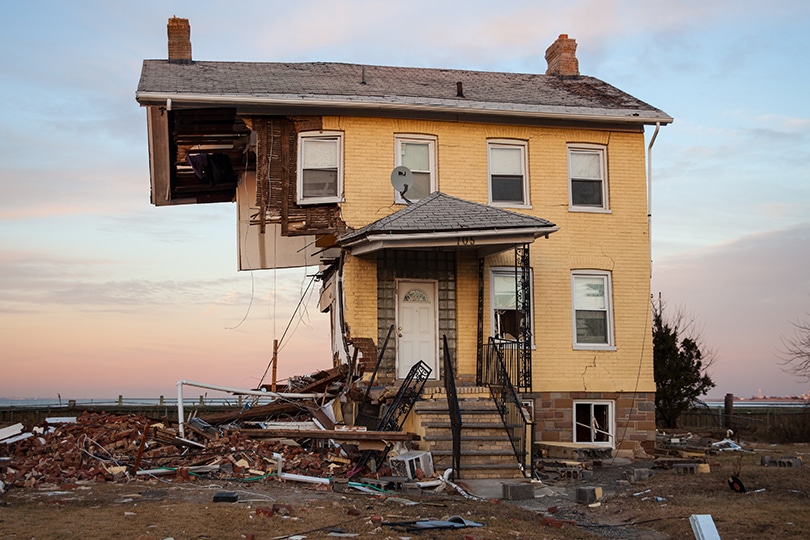 A yellow two story house with the lower left side missing, on a beach at sunset