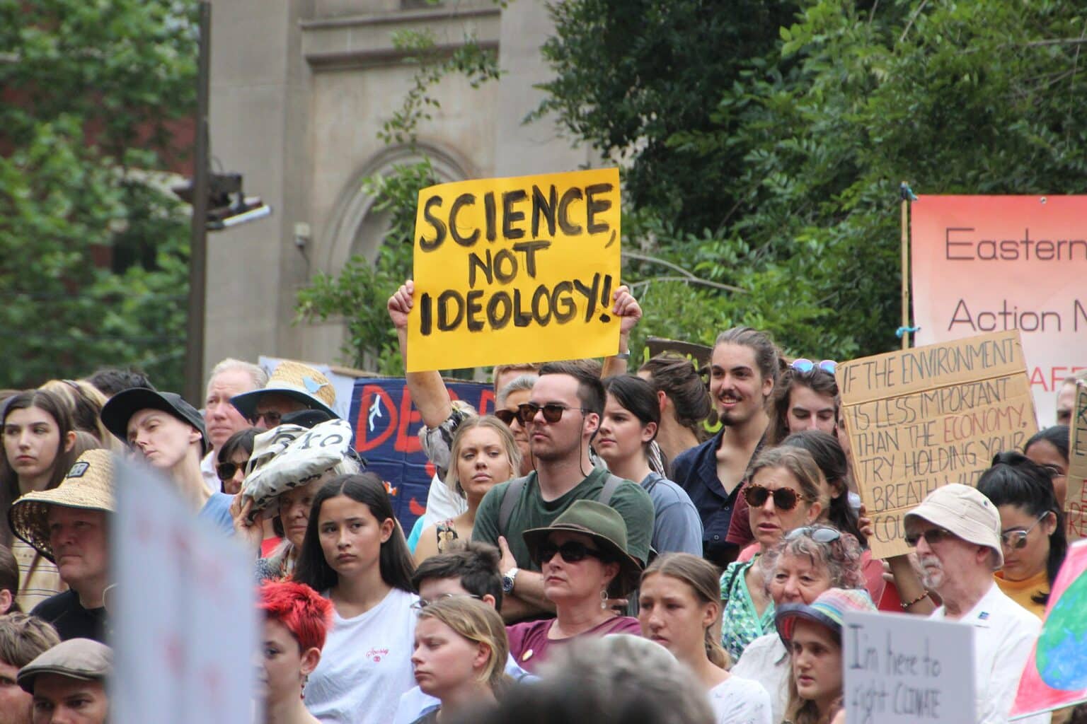 Crowd of people protesting and holding signs, including a bright yellow poster with black text 'Science not ideology'