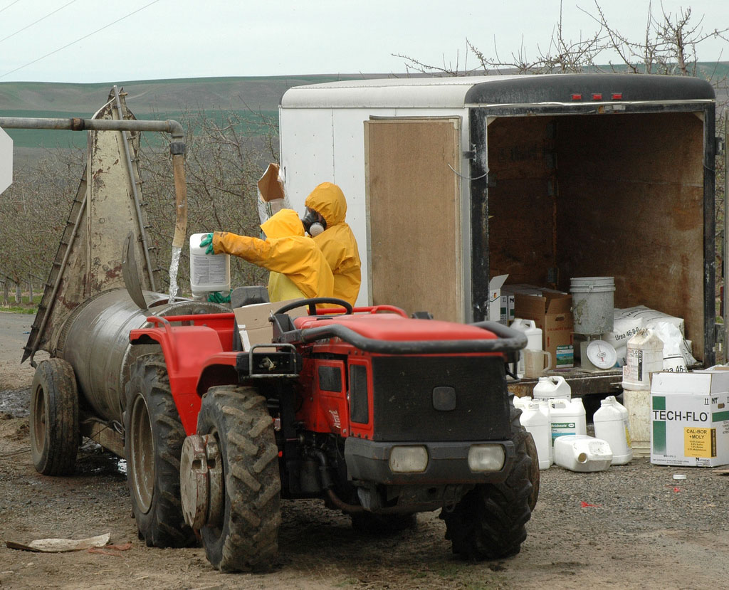 farmworkers load agrochemicals into a sprayer to be applied to crops