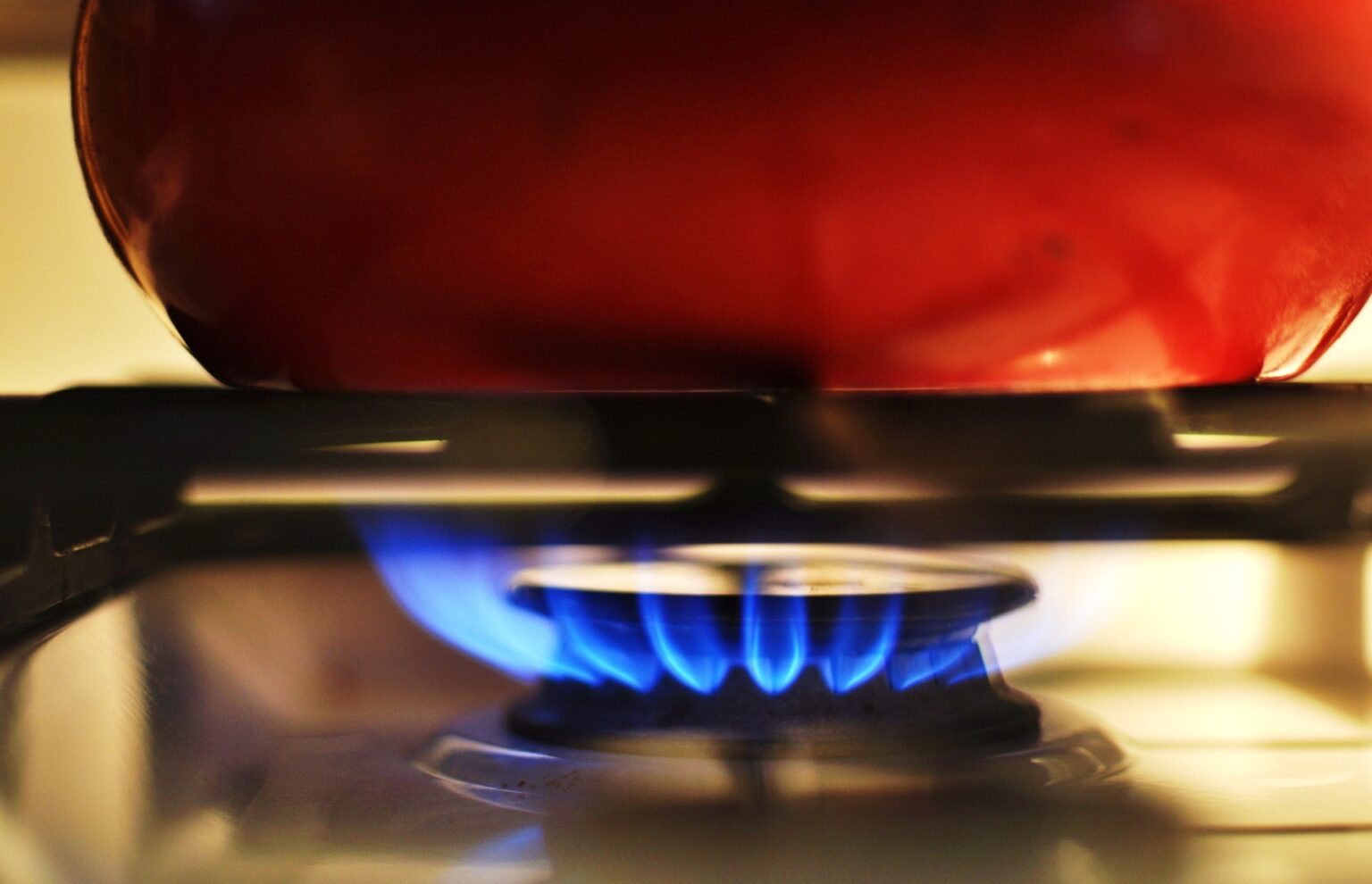 Bottom of red cooking pot sitting on a gas stove with blue flames