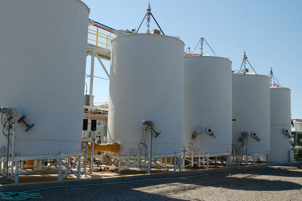 Five large white industrial tanks in a row, connected by piping