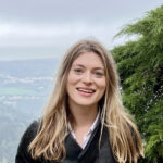 Cartie Werthman, a young woman with straight blonde hair, smiling in front of an evergreen tree and aerial view of a city