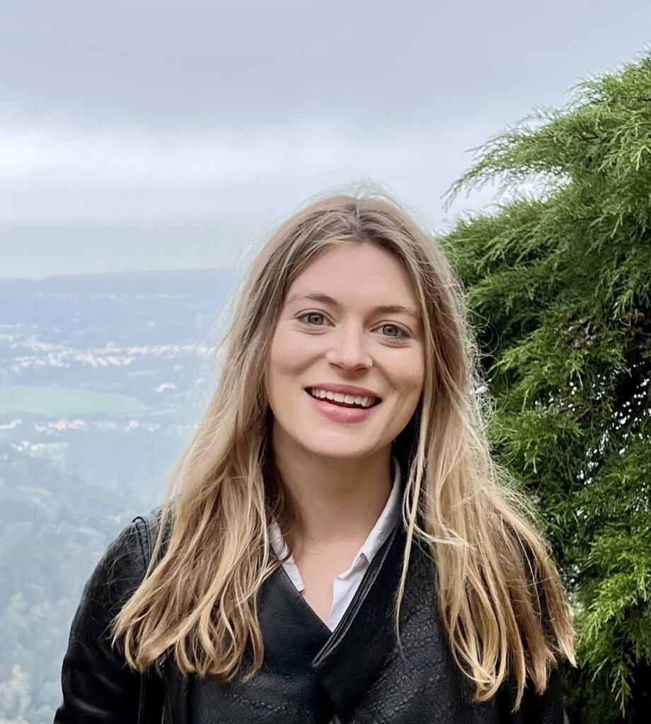 Cartie Werthman, a young woman with straight blonde hair, smiling in front of an evergreen tree and aerial view of a city