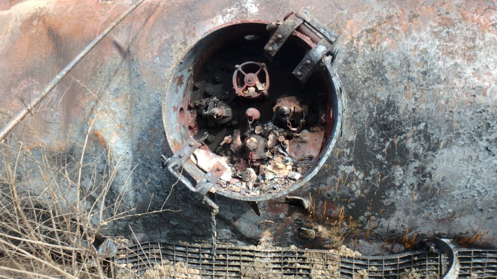 A Norfolk Southern tank car with missing aluminum protective housing cover and metallic debris contained within the protective housing in East Palestine, Ohio.
