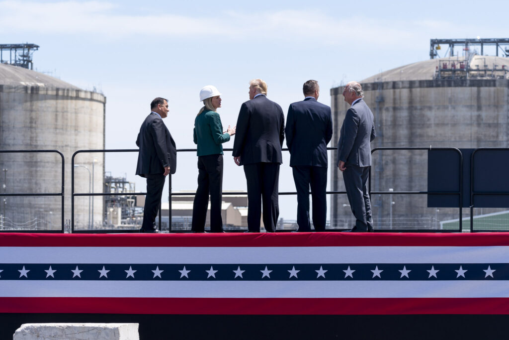 Four people standing around President Donald Trump on a raised platform looking at the giant storage tanks at Cameron LNG Export Terminal.