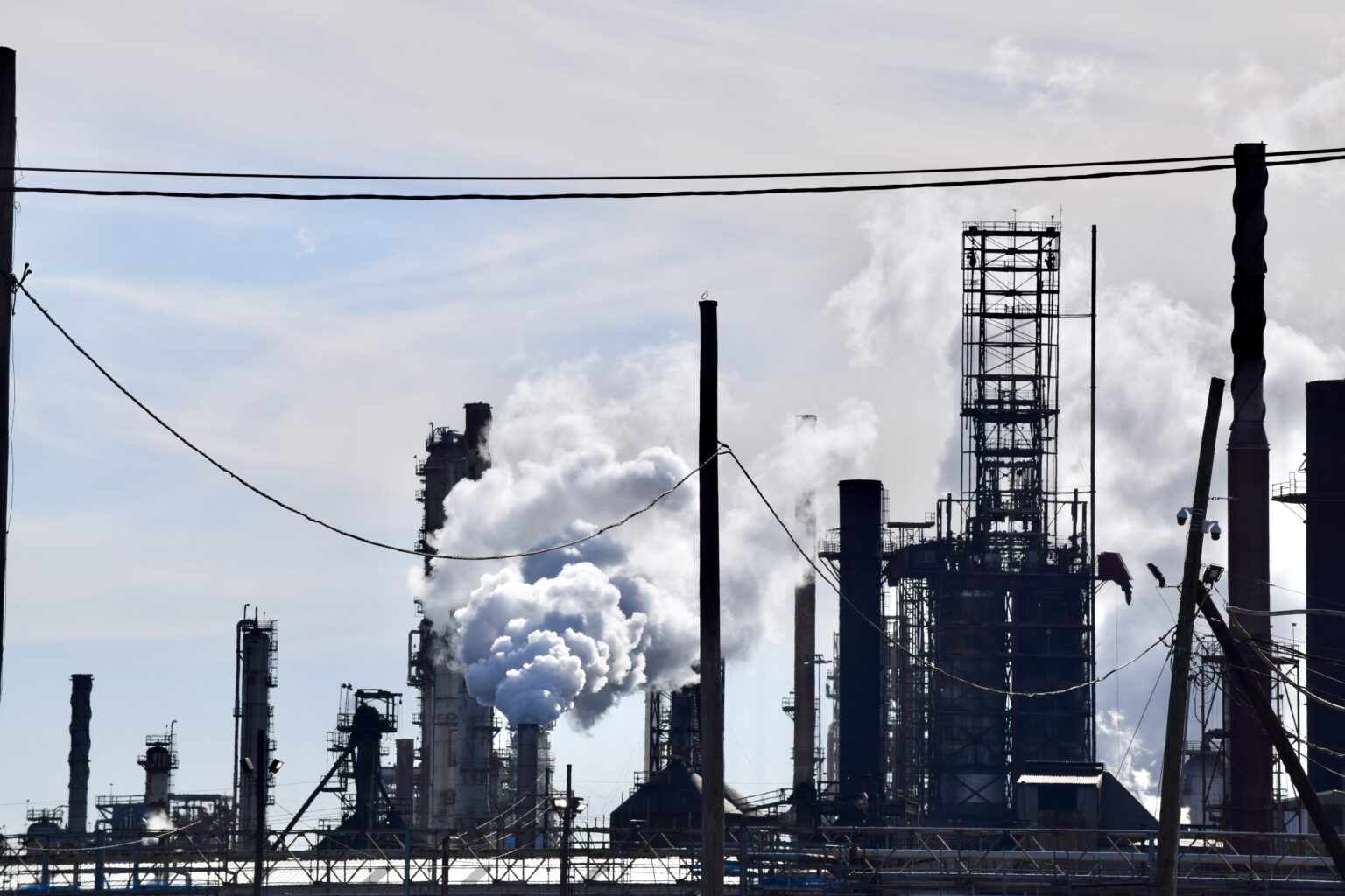 White smoke billows out of several dark smokestacks on a zoomed-in view of an industrial chemicals facility.