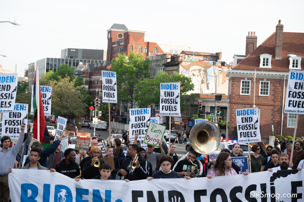 Climate activists march through Washington DC holding a long banner and placards saying 'Biden, End fossil fuels.'