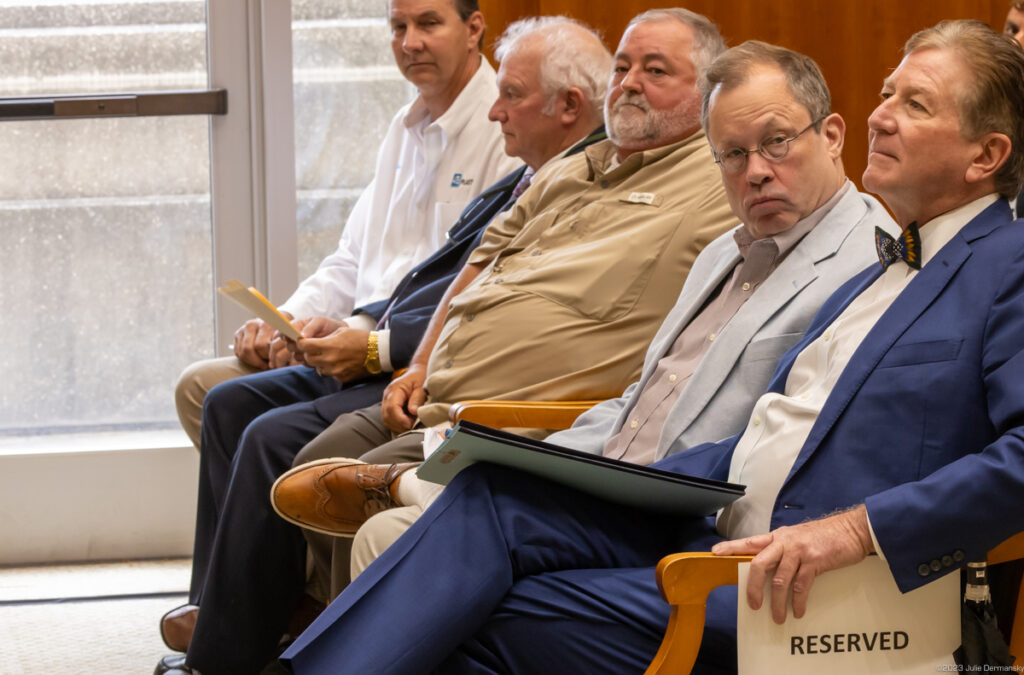 Five men sit in a row of chairs marked 'reserved'