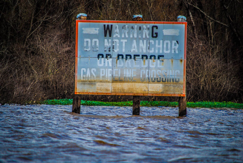 A weathered sign in the Atchafalaya Basin that reads "warning do not anchor or dredge gas pipeline crossing"