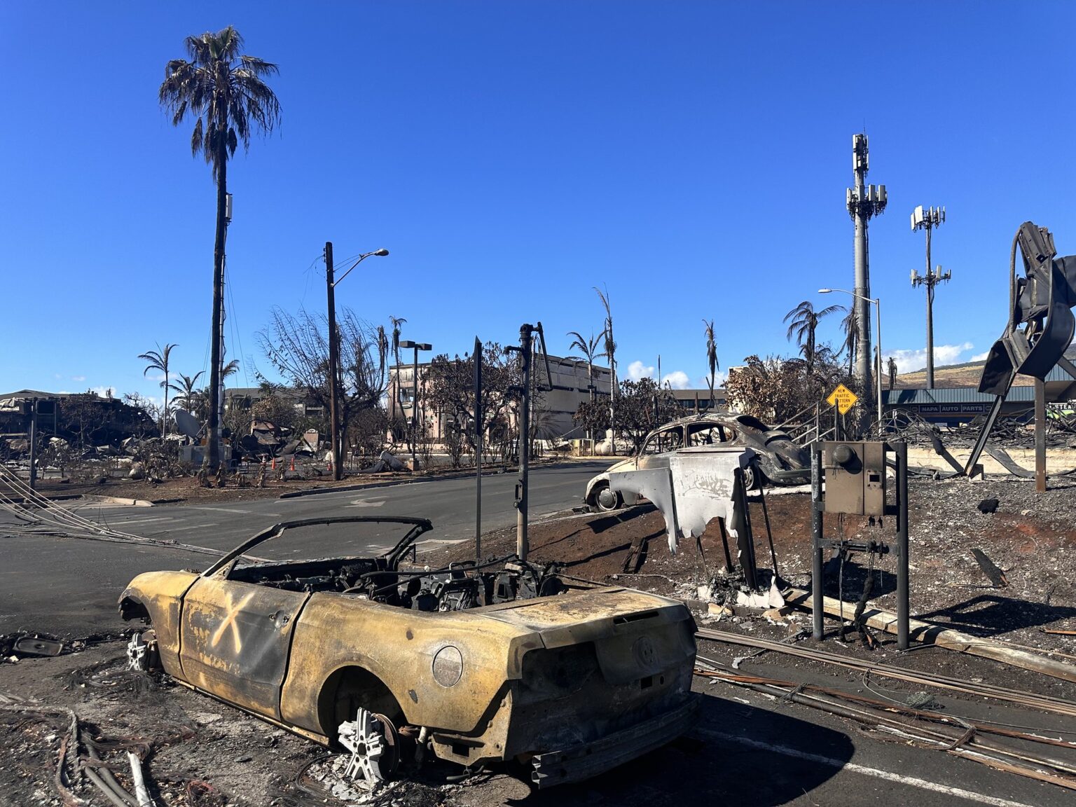 A burned car sits in the turning lane of a street in Lahaina. The "X" indicates that search and rescue personnel have checked whether any victims of the fire were inside.